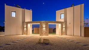 Un edificio moderno con un arco centrale in pietra, due ali laterali e un vialetto sterrato che conduce all'ingresso.