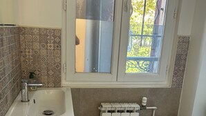 Un baño con un lavabo blanco, un inodoro, una ventana con vistas a zonas verdes y un radiador.