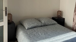 Un dormitorio con cama, dos mesitas de noche, una puerta y una lámpara colgante.