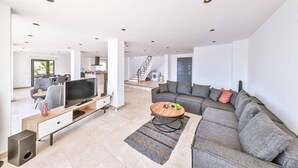 A spacious living room with a large grey sofa, a flat-screen TV, a coffee table, and a staircase leading to another level.