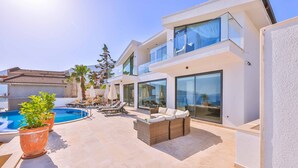 A modern two-story house with a swimming pool, outdoor seating, and large windows.