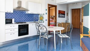 A compact kitchen with white cabinets, a microwave, stove, and oven. There is a dining area with a table and chairs. - Beach House AcquaMarina (Letojanni)