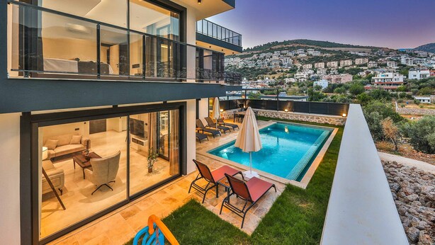 Une maison moderne à deux étages, dotée d’une piscine, d’un espace de détente extérieur et offrant une vue sur une ville située sur une colline.