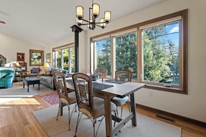 A spacious living room with a dining area, large windows, and a chandelier. - Waterfront! New Construction The Resting Place (Sturgeon Bay)