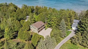 An aerial view of a property with a house surrounded by dense forest, a clear view of the ocean, and a paved driveway. - Waterfront! New Construction The Resting Place (Sturgeon Bay)