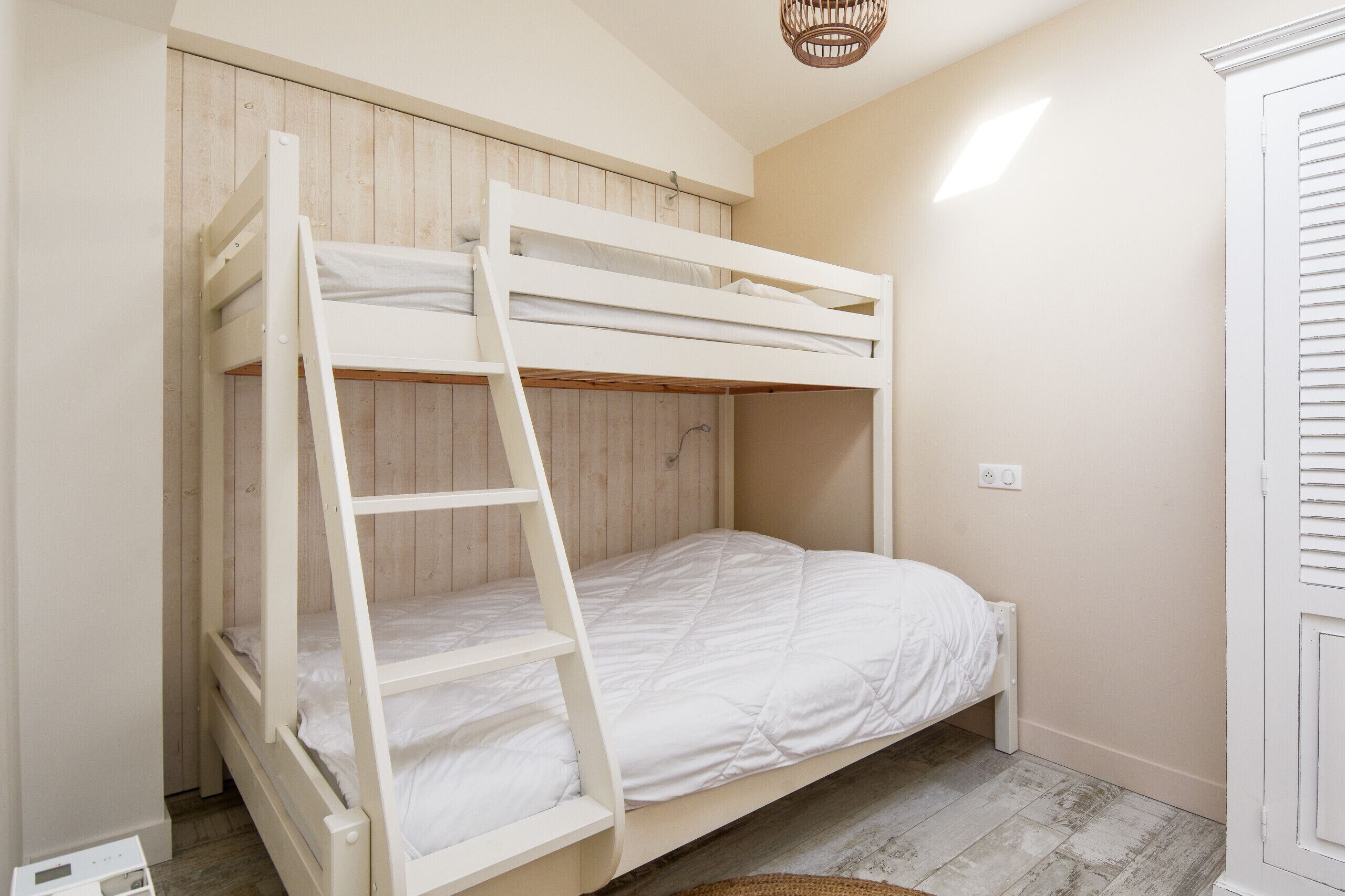 Ein Stockbett mit einer Leiter, Holzwandverkleidung und einem hellen Boden.