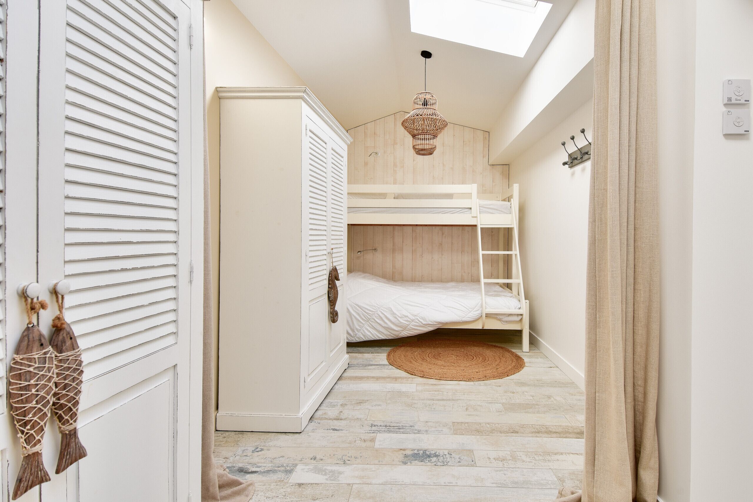 Une chambre avec un lit superposé, une armoire, un luminaire suspendu et une vue sur l’extérieur.
