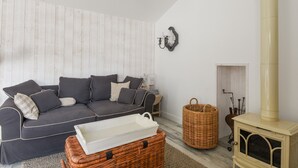 A cozy living room with a dark grey sofa, a white tray, a wicker basket, and a cream-colored wood-burning stove. - House for 6 in the heart of Bretignolles-sur-Mer (Bretignolles-sur-Mer)
