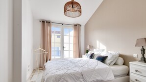 A bedroom with a bed, a nightstand, a lamp, a hanging light fixture, a window with curtains, and a view of the outside. - House for 6 in the heart of Bretignolles-sur-Mer (Bretignolles-sur-Mer)