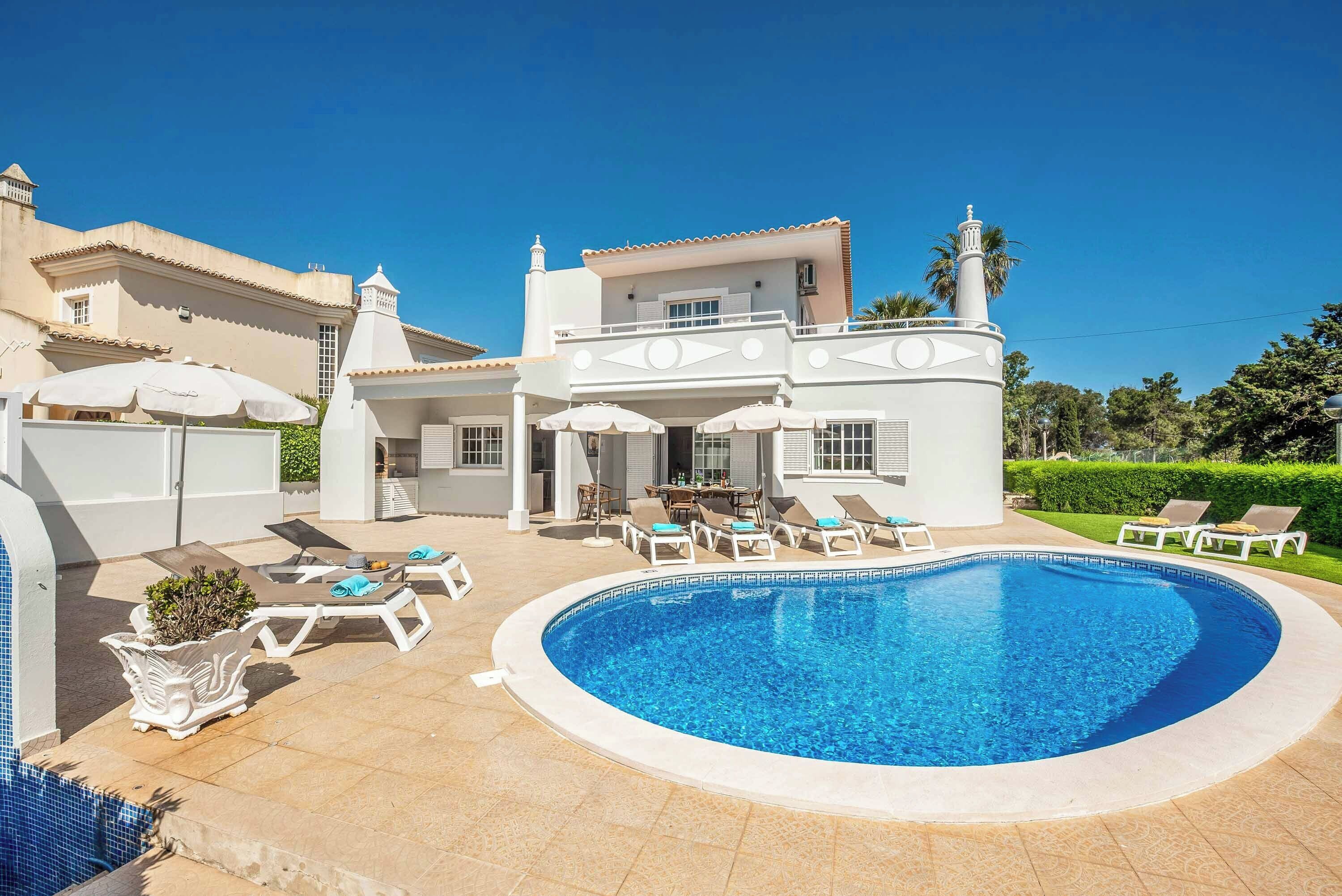 A poolside area with lounge chairs and umbrellas, a swimming pool, and a building with a balcony.