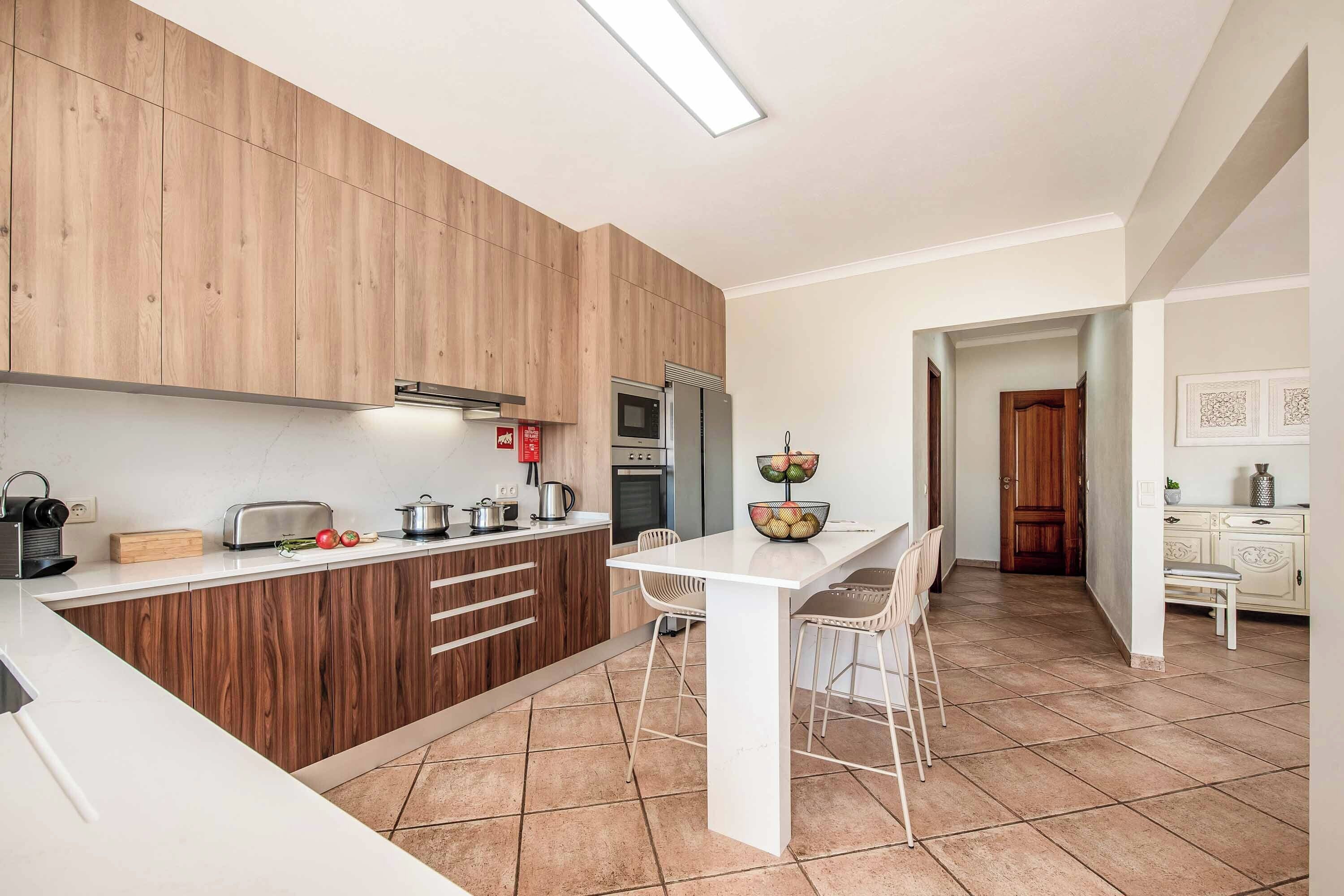 A modern kitchen with wooden cabinets, a white countertop, and a dining area with a white table and chairs.