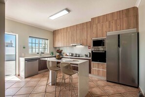 A modern kitchen with wooden cabinets, a stainless steel refrigerator, a microwave, and a dishwasher. There are two chairs at a small island.