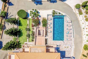An aerial view of a resort with a swimming pool, sun loungers, and a well-maintained lawn.
