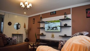 A living room with a flat-screen TV mounted on the wall, a chandelier, and a fireplace.