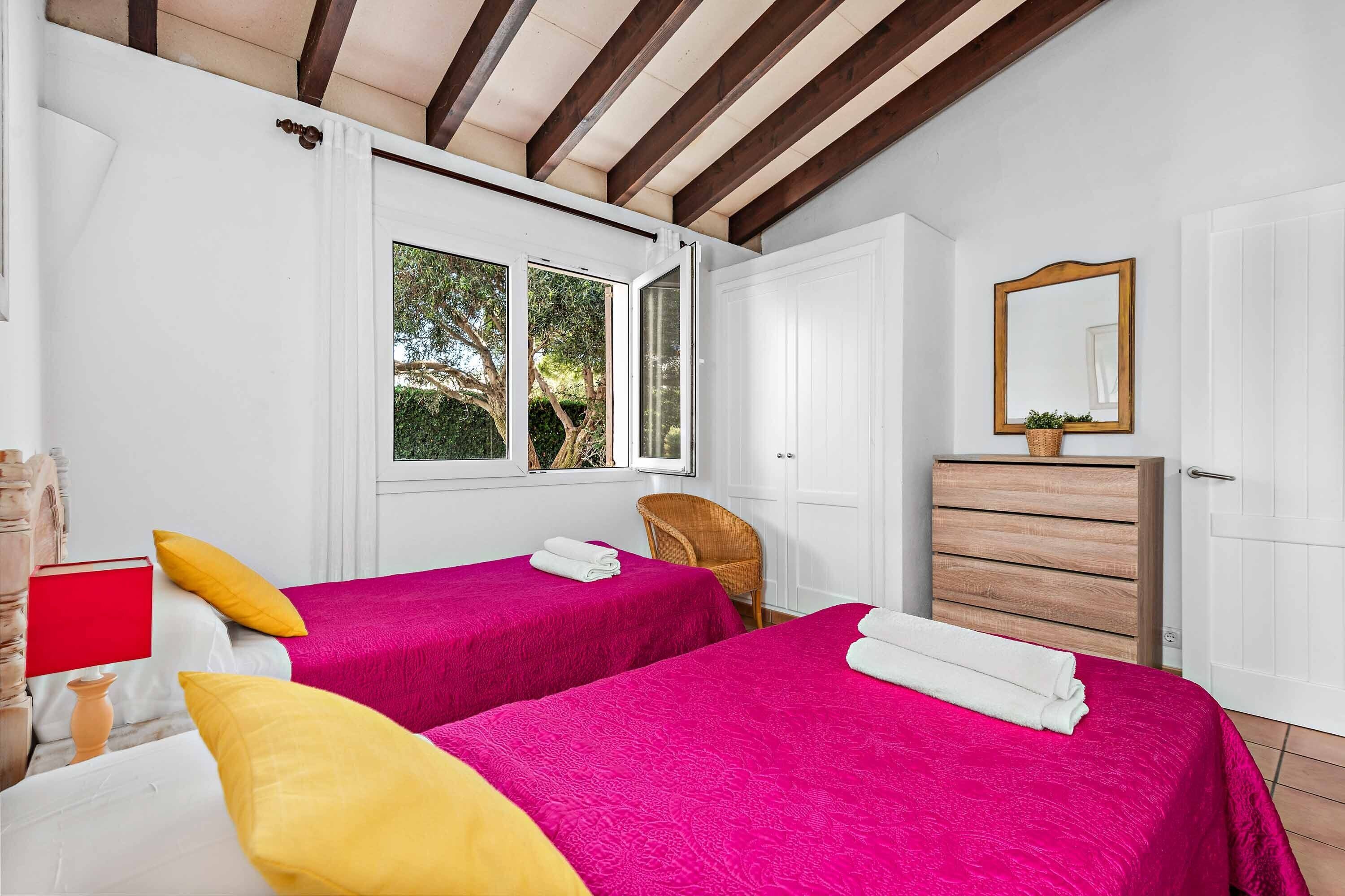 A bedroom with two beds, a wooden dresser, a mirror, and a window with a view of greenery.