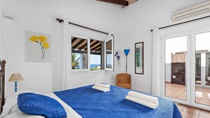 Een slaapkamer met een bed, een stoel, een raam en een deur die uitkomt op een balkon.