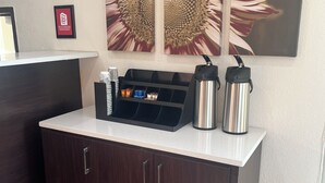 Un mostrador de recepción con una estación de café, un cartel enmarcado y una gran obra de arte con girasoles en la pared.