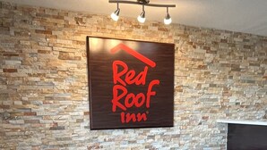 Un espace d’accueil d’un hôtel Red Roof Inn, avec un mur en pierre en arrière-plan, deux fauteuils en cuir, une petite table ronde et un luminaire au plafond.