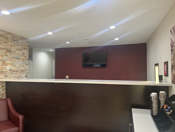 A reception area with a stone wall, a dark wooden counter, and a flat-screen TV mounted on the wall. - Red Roof Inn Haltom City (Haltom City)