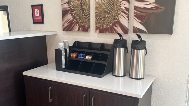 En receptionsdisk med en kaffestation, en inramad skylt och ett stort konstverk med en solros på väggen.