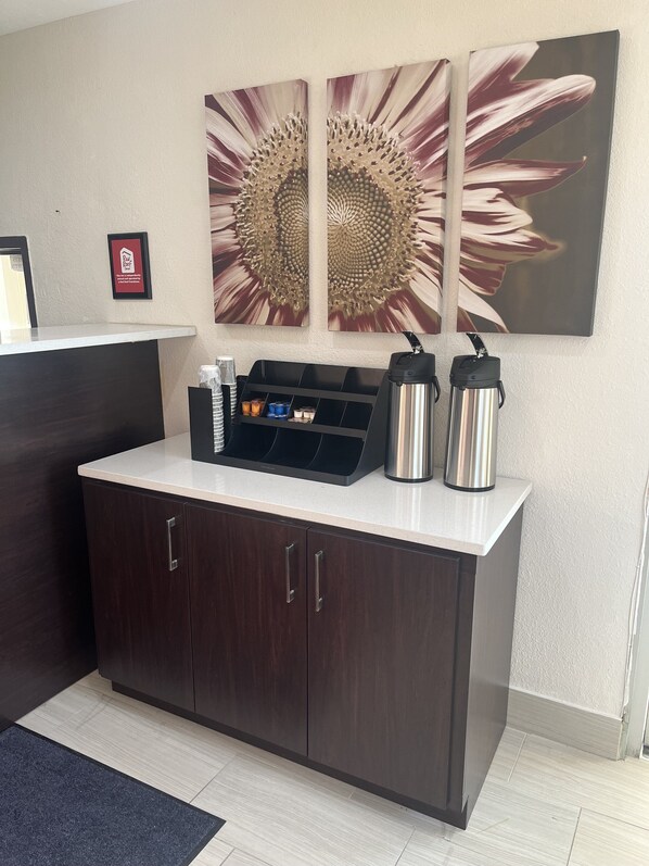 A reception desk with a coffee station, a framed sign, and a large sunflower artwork on the wall. - Red Roof Inn Haltom City (Haltom City)