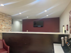 A reception area with a counter, a TV mounted on the wall, and a seating area with a chair. - Red Roof Inn Haltom City (Haltom City)