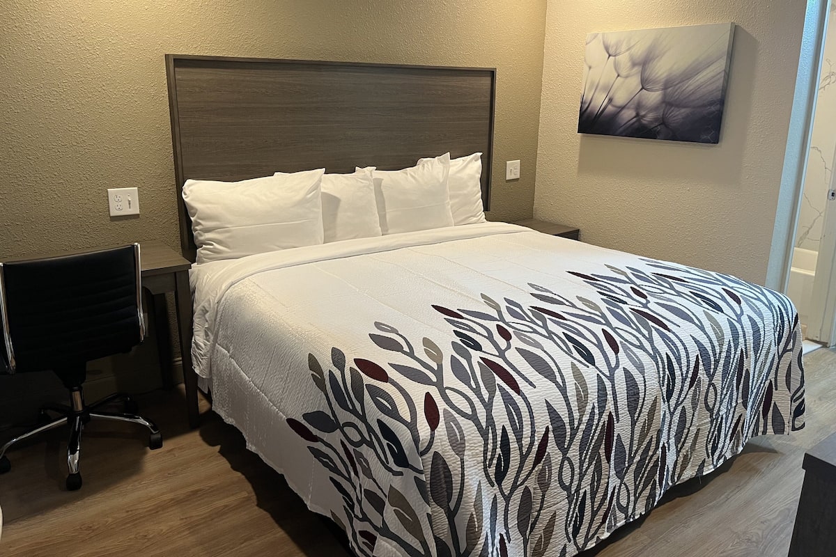 Een netjes opgemaakt bed met een bedsprei met dessin, een houten hoofdbord en een aan de muur hangend schilderij.