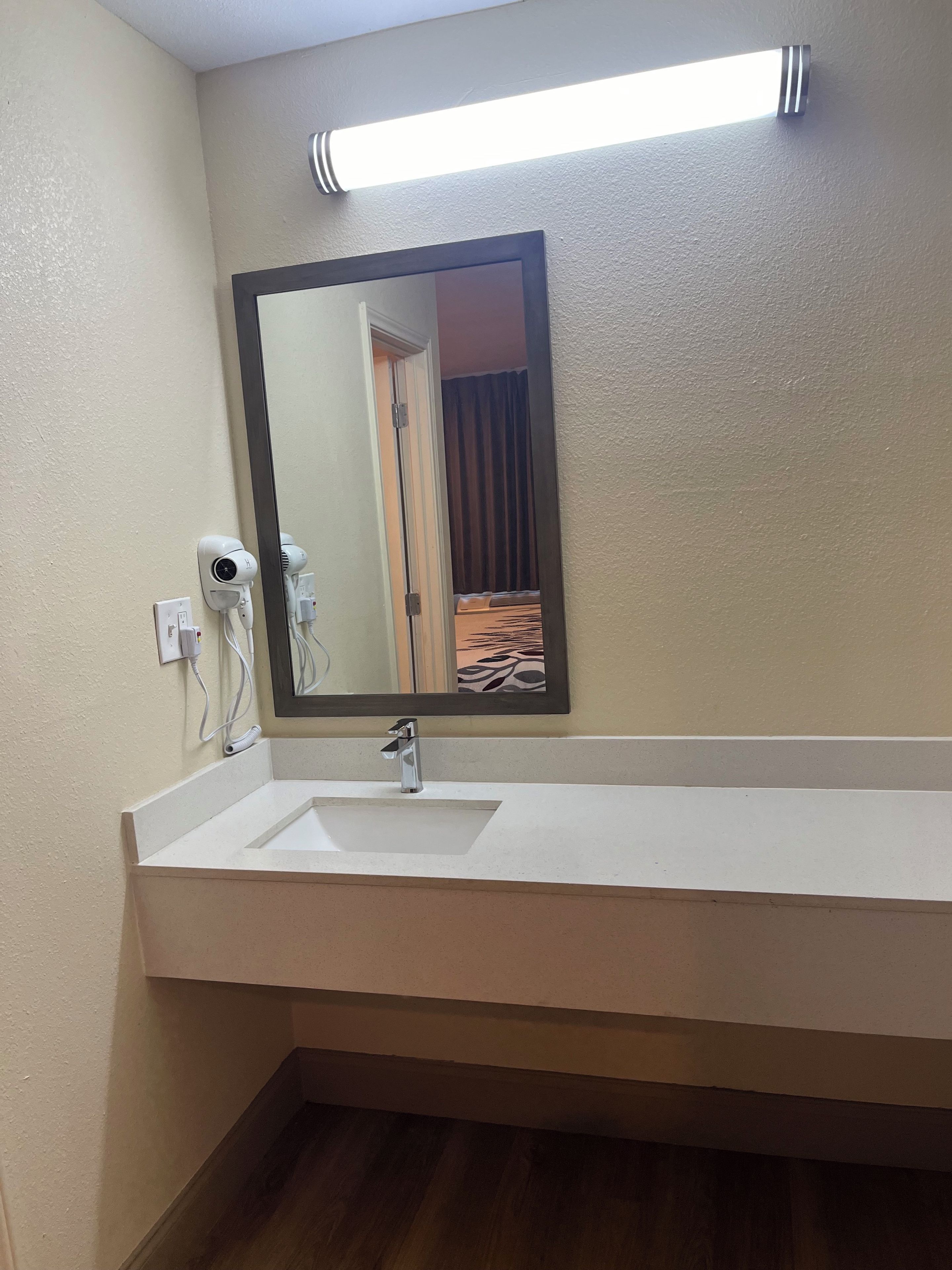 A bathroom with a white sink, a mirror, and a hairdryer on the wall.