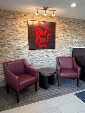 Een Red Roof Inn receptiegedeelte met een achtergrond van een stenen muur, twee leren fauteuils, een klein rond tafeltje en een plafondlamp.