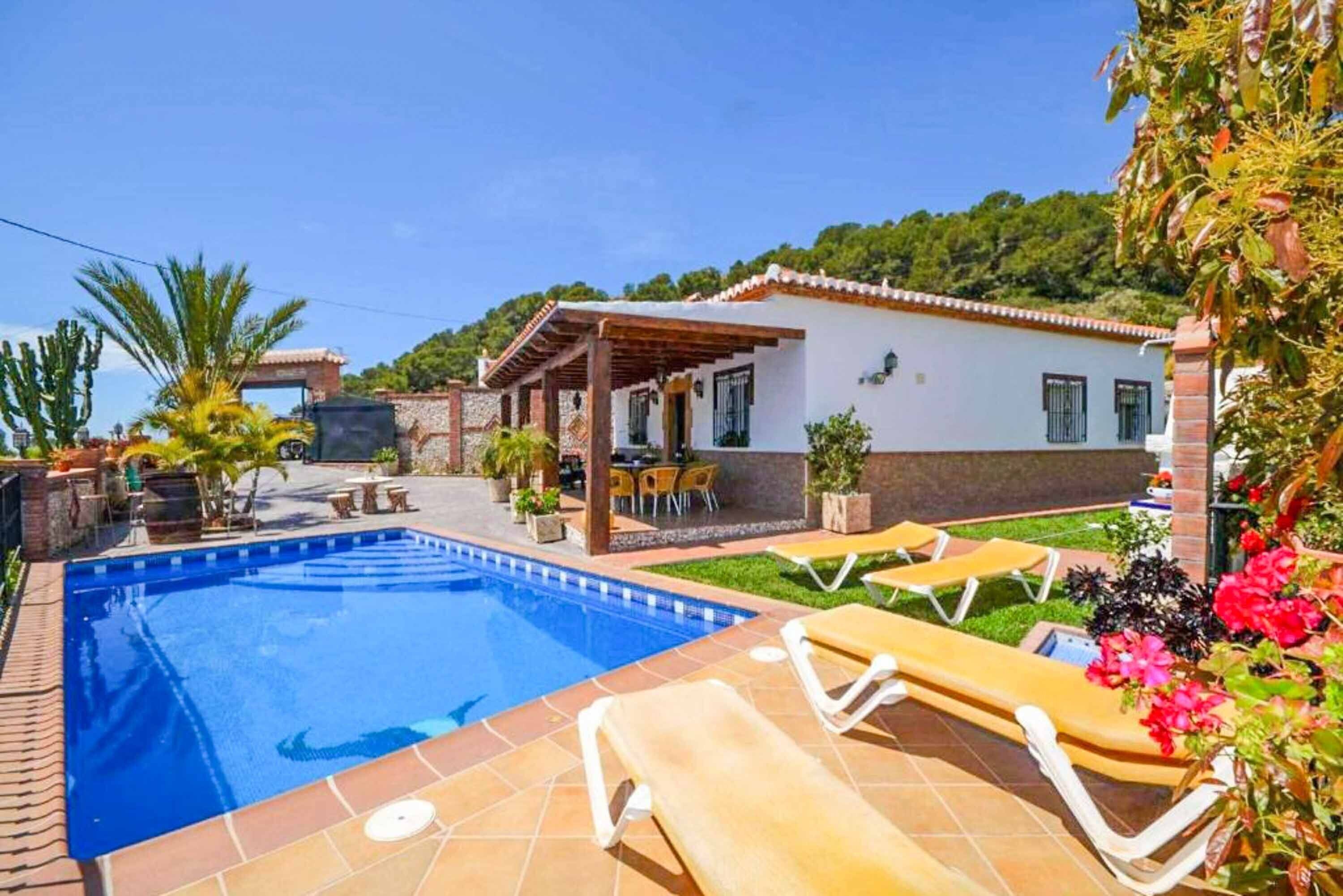 A swimming pool with lounge chairs, a covered patio, and a garden area.