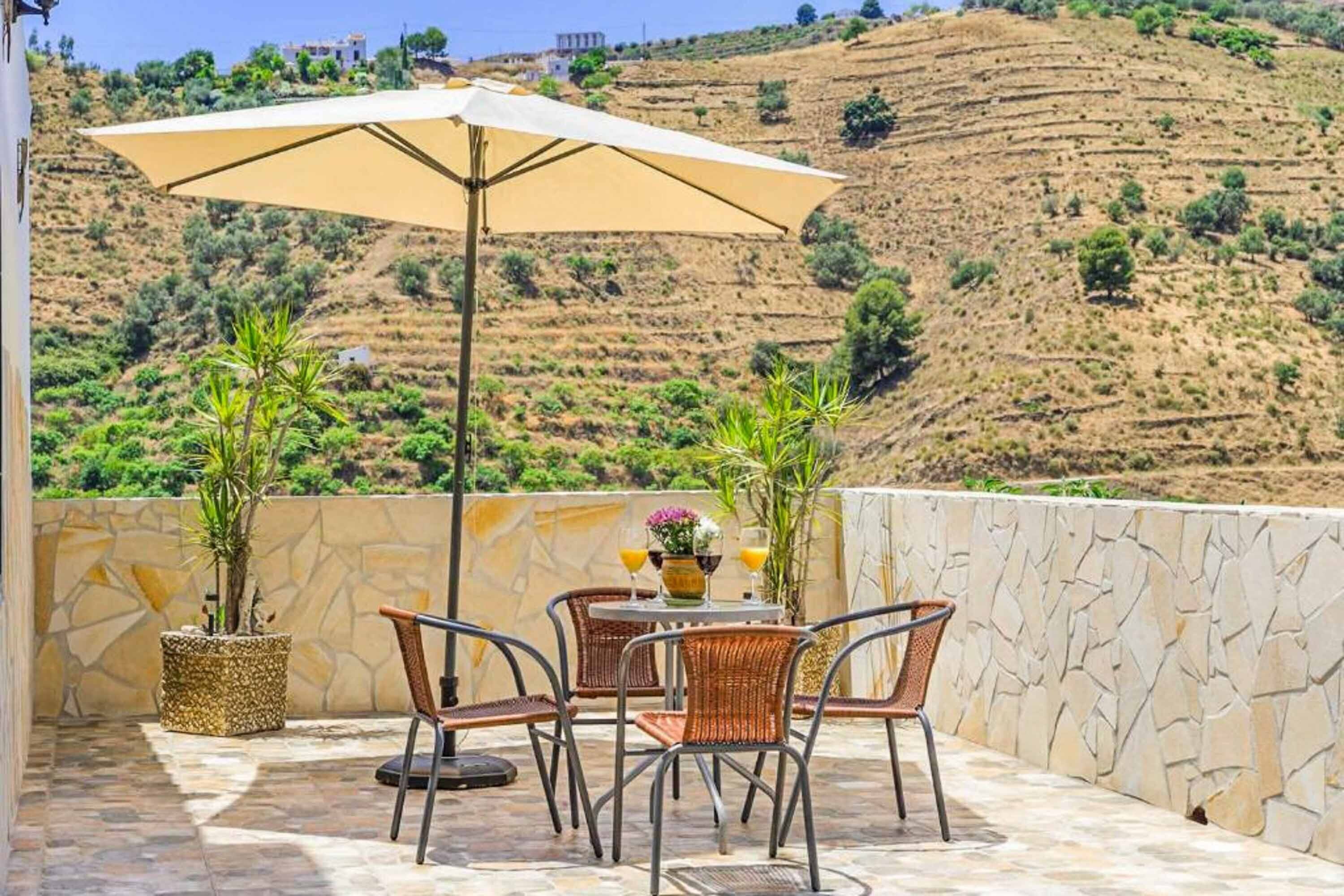 An outdoor patio with stone flooring, wicker chairs, a table with a vase and glasses, and a large umbrella.
