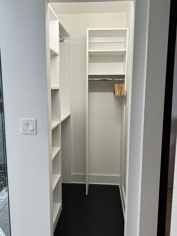 A walk-in closet with white shelving, a hanging rod, and a black floor.