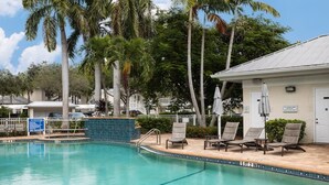 Une piscine entourée de palmiers et d’un bâtiment portant une enseigne, avec des chaises longues et des parasols à proximité.