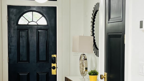 Un couloir avec une porte noire, un mur blanc et un luminaire au plafond.