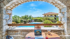 Un arco de piedra que da acceso a una zona de piscina con una computadora portátil, gafas y una vela sobre una mesa.
