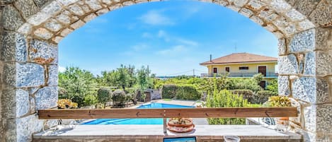 A stone archway leading to a pool area with a laptop, glasses, and a candle on a table.