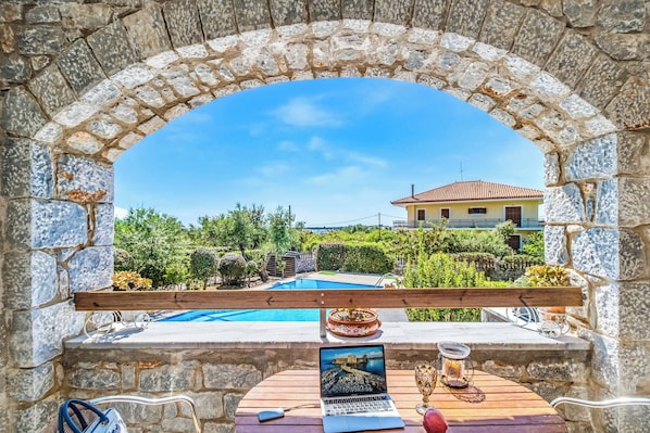 A stone archway leading to a pool area with a laptop, glasses, and a candle on a table.