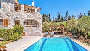 Un edificio de piedra con piscina, mobiliario exterior y una pérgola.