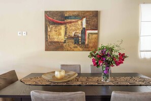 A dining area with a table, chairs, a vase with flowers, and a painting on the wall. - Villa Mandarin Platanias (Platanias)