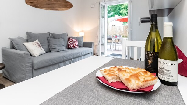 Ein modernes Wohnzimmer mit einem grauen Sofa, einem Esstisch mit Brot und zwei Weinflaschen.