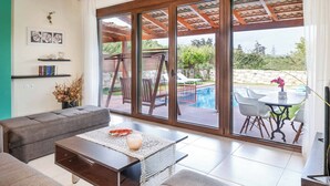 A modern living room with a sofa, coffee table, and a view of an outdoor pool area. - Villa Portokalia Platanias (Platanias)