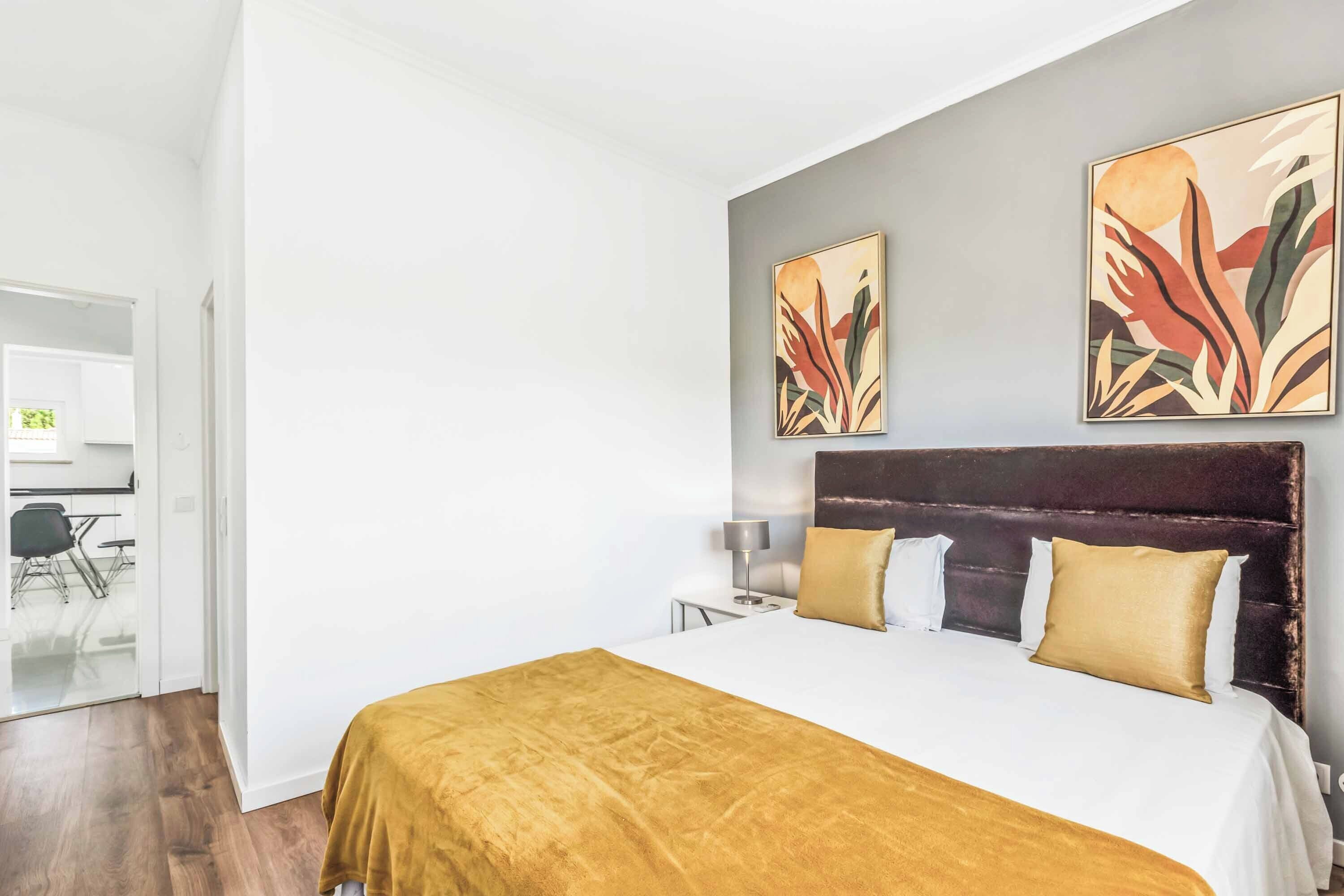A modern hotel room with a large bed, a dark headboard, and abstract wall art.
