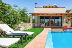 Ein modernes Haus mit Swimmingpool, einer Terrasse mit Liegestühlen und einer Steinmauer.