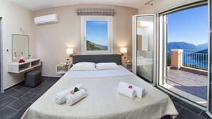 Een hotelkamer met een groot bed, een balkon met uitzicht op zee en een raam met uitzicht op de heuvels.