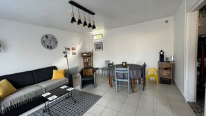 Una sala de estar con un sofá, una mesa de centro, una mesa de comedor con sillas, una estantería y un reloj en la pared.