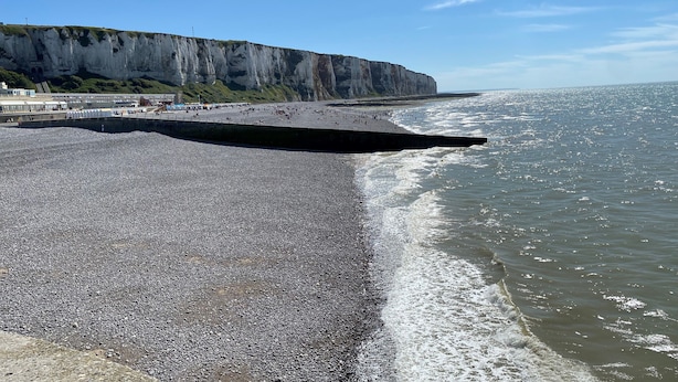 Una playa de guijarros con un acantilado al fondo.