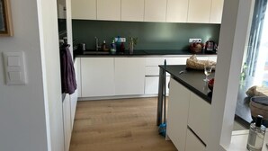 A modern kitchen with white cabinets, a black countertop, and a wooden floor. - Location Maison Carnac Plage (CARNAC PLAGE)