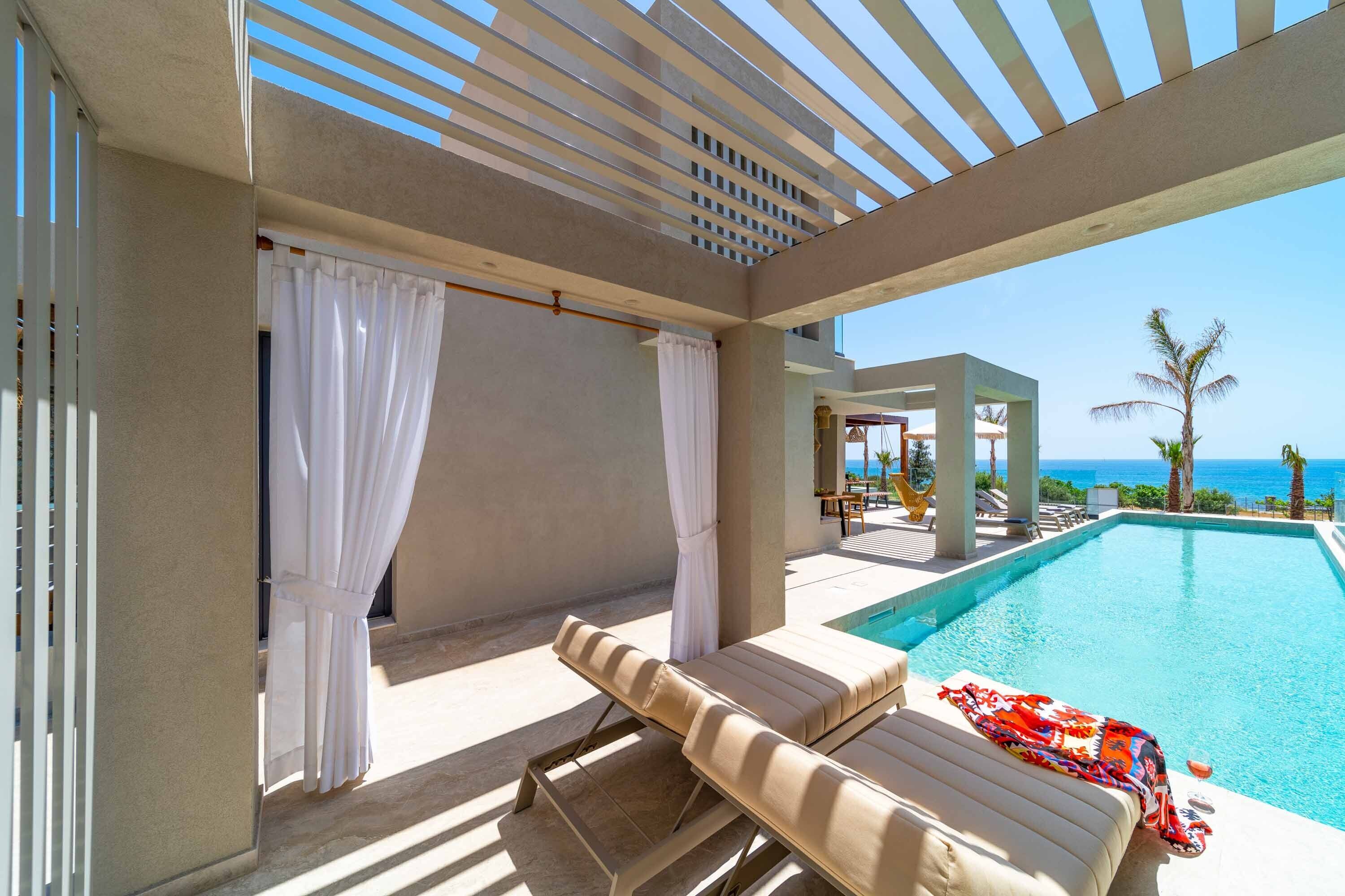 A poolside area with two lounge chairs, a covered seating area, and a view of the ocean.