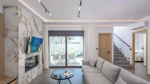 Un salon moderne doté d’une cheminée en marbre, d’un grand canapé et d’un coin repas offrant une vue sur l’extérieur.