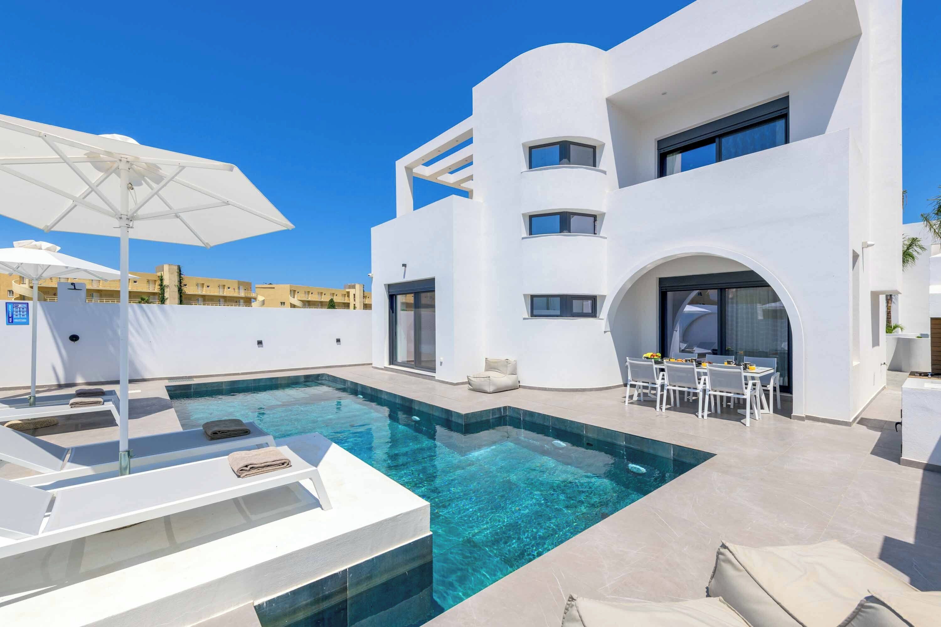 A modern pool area with lounge chairs and a dining table.